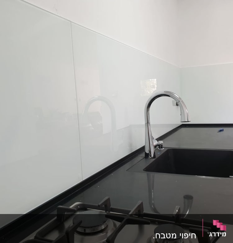 זכוכית שקופה על קיר מטבח מעל כיור וברז